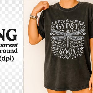 May include: Dark gray t-shirt with a white dragonfly design and the words "GYPSY SOUL". The design is surrounded by floral elements. The shirt has short sleeves and a relaxed fit.