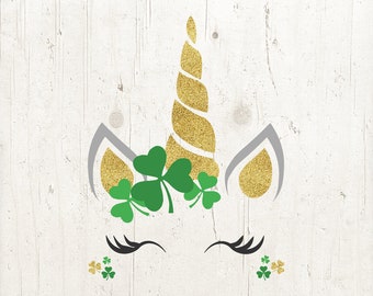 May include: A white unicorn with a gold glitter horn and shamrock leaves. The unicorn has closed eyes and a gray glitter ear on each side of its head. The background is a white woodgrain texture.