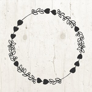 May include: A black wreath with a circle of hearts and leaves. The wreath is on a white wood background.
