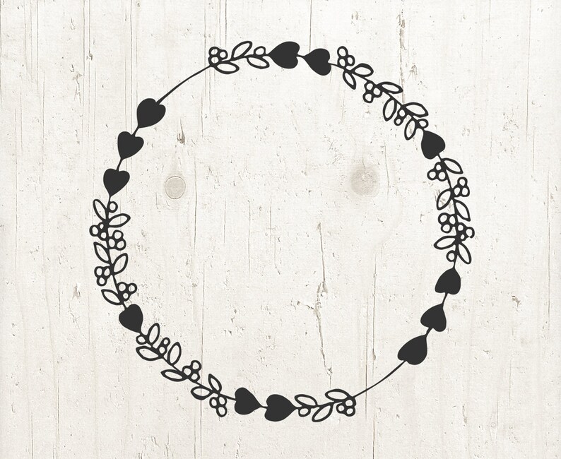 May include: A black wreath with a circle of hearts and leaves. The wreath is on a white wood background.