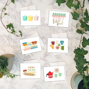 May include: A collection of greeting cards featuring retro kitchen-themed illustrations. Designs include sugar, coffee, and tea canisters, baking dishes, mugs, a teapot, and kitchen utensils. The cards are on a marble surface with greenery.