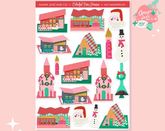 May include: A sheet of colorful Christmas-themed stickers featuring various houses, a snowman, Santa Claus, and a candle. The stickers are designed in a retro style with pink, red, and green colors. The text "Amaya Jade and Co. Colorful Putz Houses Not Waterproof" is printed at the top of the sheet.