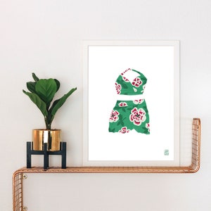 May include: A white framed print of a green and pink floral swimsuit with a halter top and a skirt.