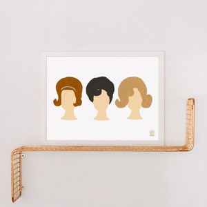 May include: A white framed print with three stylized illustrations of women's hairstyles from the 1960s. The hairstyles are brown, black, and blonde. The print has the text "Jen Hall" in the bottom right corner.