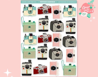 May include: A sticker sheet featuring various vintage camera designs in a variety of colors, including teal, red, pink, and gray. The cameras have a retro aesthetic, with details like rainbow stripes and the word "Vintage" on some. The sheet is labeled "Vintage Cameras."