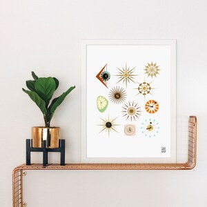 May include: A white framed print with a white background featuring a collection of 12 mid-century modern style clocks in various shapes and colors. The clocks are all in the shape of stars, circles, and triangles. The print is on a shelf with a potted plant.