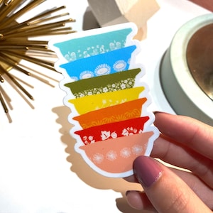 May include: A sticker of a stack of colorful bowls with floral patterns. The bowls are stacked in a rainbow order, starting with blue and ending with pink.