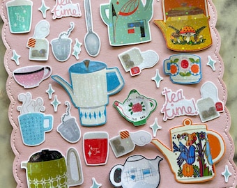 Può includere: Una tavola rosa con bordi smerlati che presenta vari adesivi a tema tè, tra cui teiere, tazze, bustine di tè, cucchiai e infusori. Gli adesivi mostrano motivi colorati, disegni floreali e il testo tea time in un carattere corsivo.