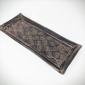 May include: A black rectangular ceramic serving tray with a raised geometric pattern of squares.