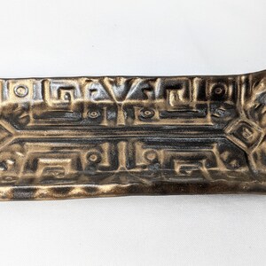 May include: A rectangular ceramic dish with a geometric design in gold and black. The dish has a raised rim and a slightly curved shape.