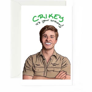 Puede incluir: Una tarjeta de felicitación blanca con una ilustración digital de una persona de cabello castaño con una camisa beige abotonada con el texto 'ROBERT' y 'AUSTRALIA ZOO' en el pecho. Sobre la figura, el texto verde dice 'CRIKEY It's your birthday!'