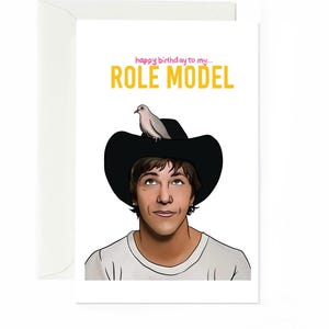 May include: A white greeting card featuring a cartoon illustration of a person wearing a black cowboy hat with a small grey bird perched on top. The text above the illustration reads, "happy birthday to my... ROLE MODEL" in pink and yellow.