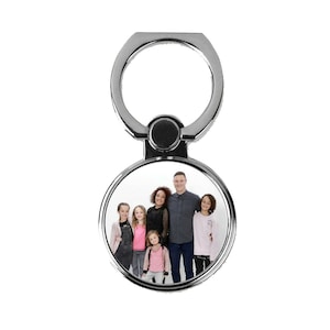 May include: A silver phone ring holder with a round photo insert featuring a family of six. The photo shows a man, a woman, and four children.