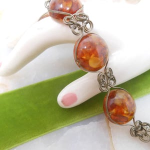 May include: A silver wire bracelet with amber beads. The beads are round and have a translucent appearance, with flecks of gold visible inside.