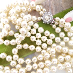 May include: A multi-strand pearl necklace with a silver clasp featuring a flower design. The pearls are white and round.