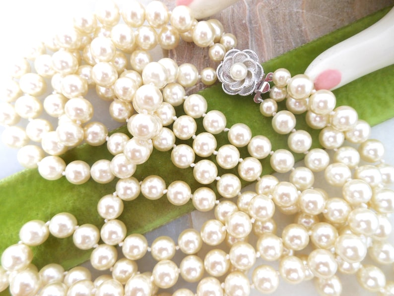 May include: A multi-strand pearl necklace with a silver clasp featuring a flower design. The pearls are white and round.
