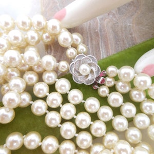 May include: A multi-strand pearl necklace with a silver flower clasp. The necklace is made of white pearls and is on a green velvet surface.
