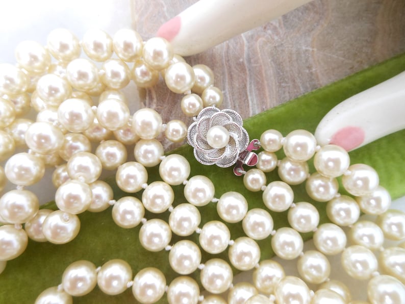 May include: A multi-strand pearl necklace with a silver flower clasp. The necklace is made of white pearls and is on a green velvet surface.