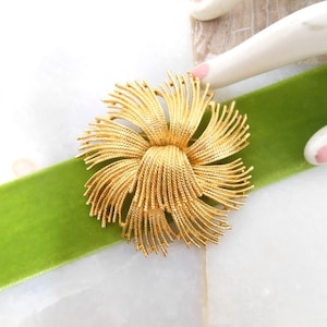 May include: A gold-toned brooch in the shape of a flower with a twisted center. The brooch is made of thin, delicate metal strands that create a radiating effect.