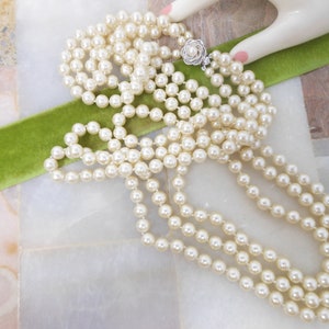 May include: A long strand of white faux pearl necklace with a silver clasp. The necklace is draped over a green velvet ribbon.