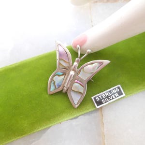 May include: A silver butterfly brooch with iridescent abalone shell wings. The brooch is on a green velvet surface and has a "STERLING SILVER" tag attached.
