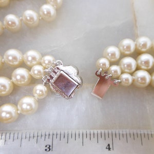 May include: A three-strand pearl necklace with a silver clasp. The necklace is measured against a ruler, showing it is approximately 18 inches long.