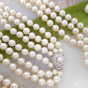 May include: A multi-strand pearl necklace with a silver flower clasp. The pearls are white and round.