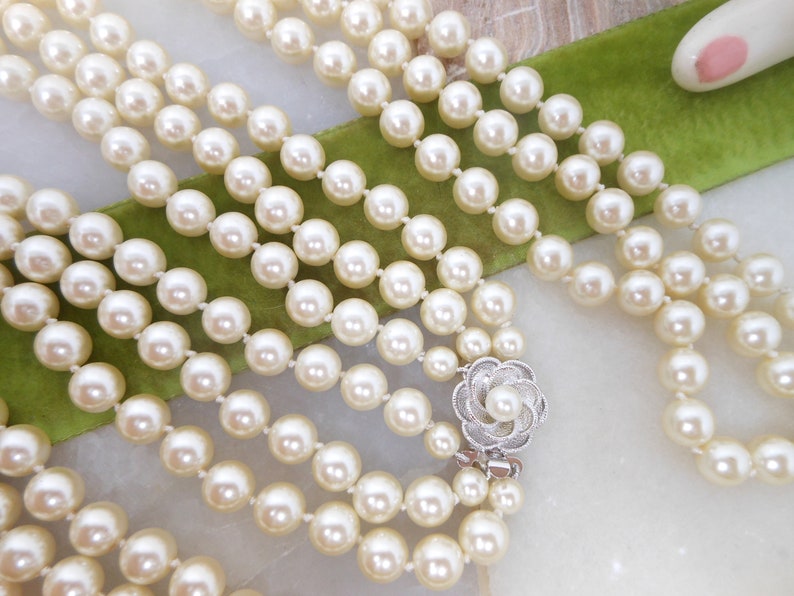May include: A multi-strand pearl necklace with a silver flower clasp. The pearls are white and round.