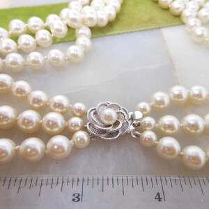 May include: A three-strand pearl necklace with a silver flower clasp. The necklace is approximately 3 inches long.