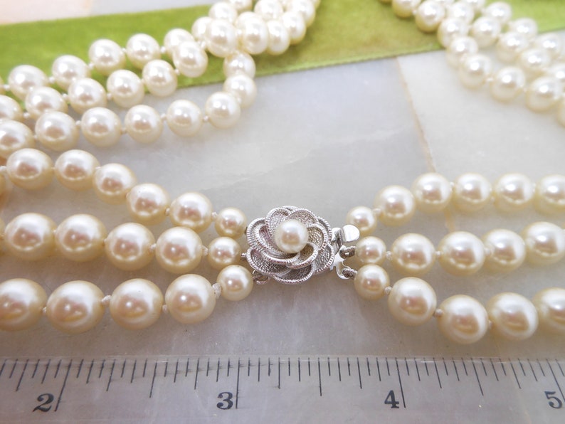 May include: A three-strand pearl necklace with a silver flower clasp. The necklace is approximately 3 inches long.