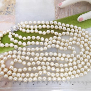 May include: A multi-strand pearl necklace with a silver clasp featuring a small flower design. The necklace is approximately 7 inches long.