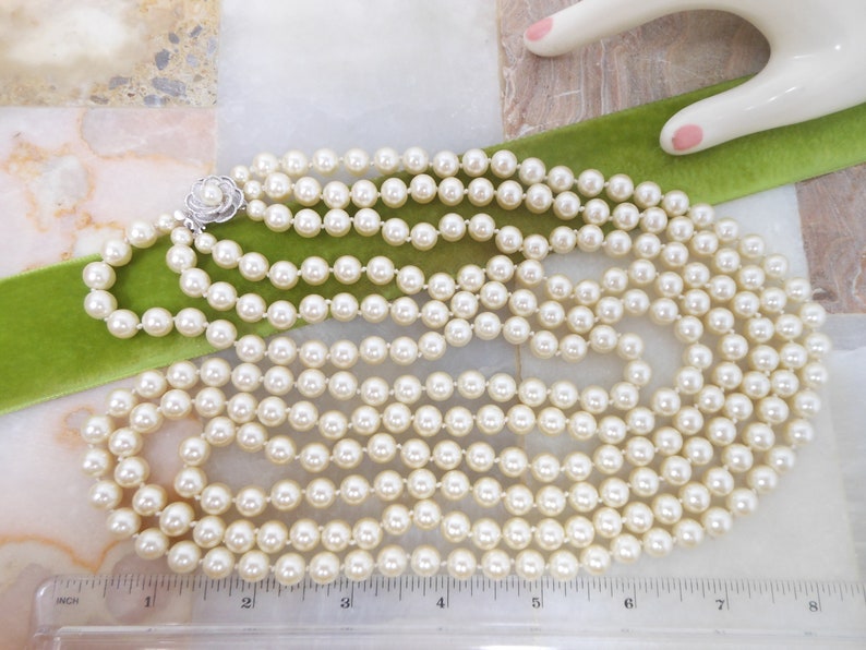 May include: A multi-strand pearl necklace with a silver clasp featuring a small flower design. The necklace is approximately 7 inches long.