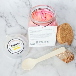 May include: A clear glass jar filled with a pink and orange whipped soap scrub. The jar has a cork lid and a label that reads "Whipped Soap + Scrub" and "Clean & Pure".