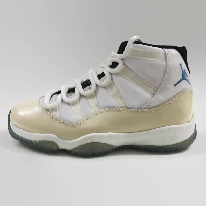 May include: White and cream colored high-top sneakers with a blue Jumpman logo on the side. The shoes have a white midsole and a translucent outsole.