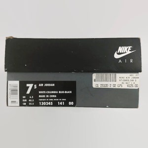 May include: A white shoebox with black text and a Nike Air logo. The box is labeled "Air Jordan" and shows the size 7.5, color "White-Columbia Blue-Black", and "Made in China".