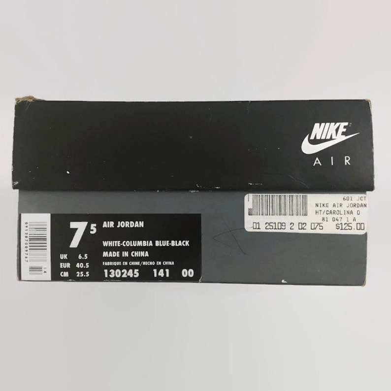 May include: A white shoebox with black text and a Nike Air logo. The box is labeled "Air Jordan" and shows the size 7.5, color "White-Columbia Blue-Black", and "Made in China".