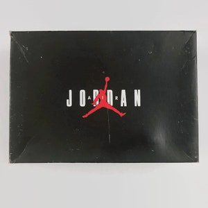 May include: A black shoebox with the word "JORDAN" in white letters and a red silhouette of a basketball player with the word "AIR" in white letters above the player.