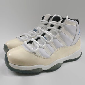 May include: White and cream colored high-top sneakers with a blue and black accent on the tongue. The sneakers have a white lace and a white sole.