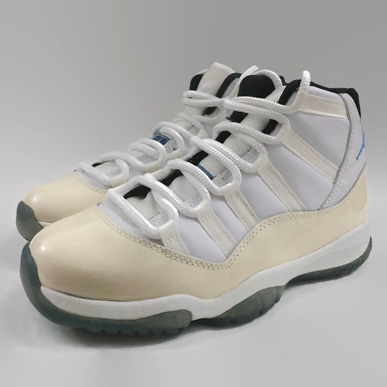 May include: White and cream colored high-top sneakers with a blue and black accent on the tongue. The sneakers have a white lace and a white sole.