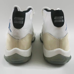 May include: A pair of white and cream-colored sneakers with a blue and black logo on the side. The sneakers have a white midsole and a gray outsole.