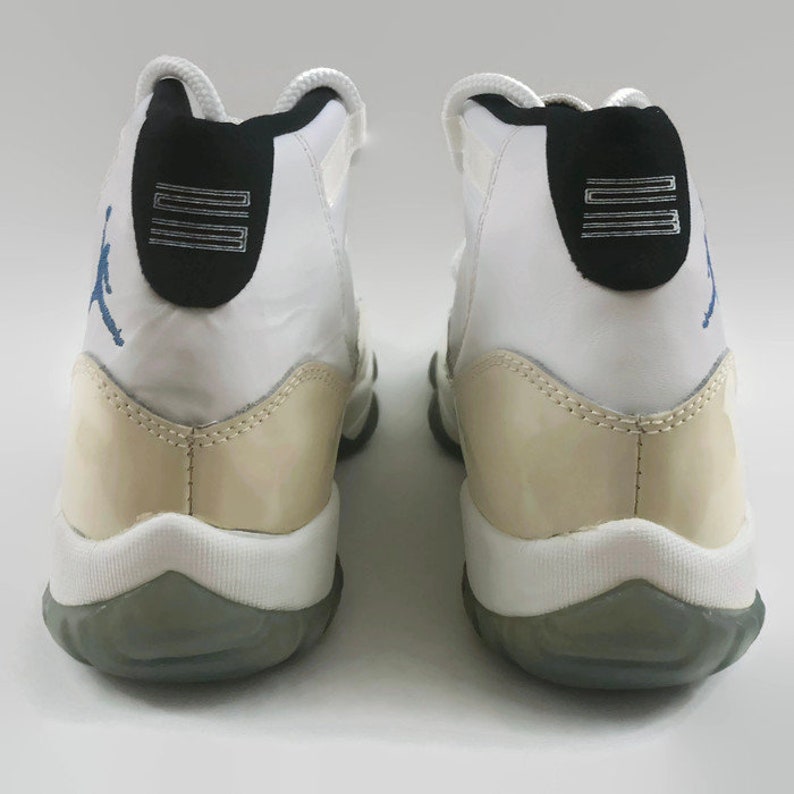 May include: A pair of white and cream-colored sneakers with a blue and black logo on the side. The sneakers have a white midsole and a gray outsole.