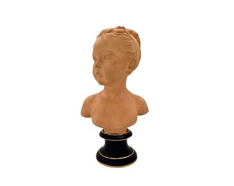 May include: Terracotta bust of a young girl with a braided bun, on a black pedestal with gold trim.