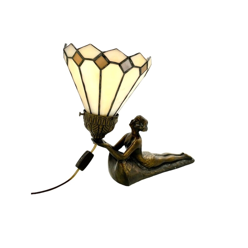 May include: A bronze lamp base in the shape of a reclining figure holding up a stained glass lampshade with a geometric pattern.