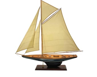 May include: A detailed model sailboat with cream-colored sails and wooden masts and hull. The boat is mounted on a dark wooden base. The hull is painted in a combination of blue and brown tones. The model is a decorative nautical item.