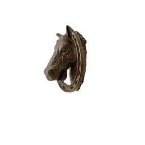 May include: A brown horse head door knocker with a horseshoe design. The knocker is made of metal and has a realistic horse head design.