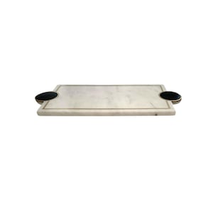 May include: A rectangular marble serving board with a gold trim and two black circular handles. The board is white with gray veining, suitable for serving appetizers or charcuterie.