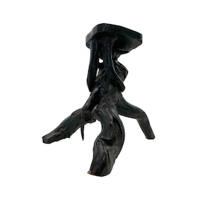 May include: Black wooden tripod stand with a flat top. The stand is made of a single piece of wood that has been carved into a unique shape.