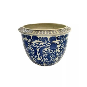 May include: A large, white ceramic planter with a blue and white floral design. The planter has a wide, round base and a slightly flared rim.