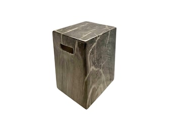 Puede incluir: Un taburete rectangular con un patrón de mármol gris y blanco en toda su superficie. El taburete tiene una parte superior plana y un pequeño recorte rectangular horizontal cerca del borde superior en el lateral, que sirve como asa para moverlo.