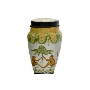 May include: A decorative ceramic jar with a lid. The jar features a cream-colored base with yellow and green accents. Two monkeys are depicted holding a tree. The lid is cream-colored with a floral pattern.